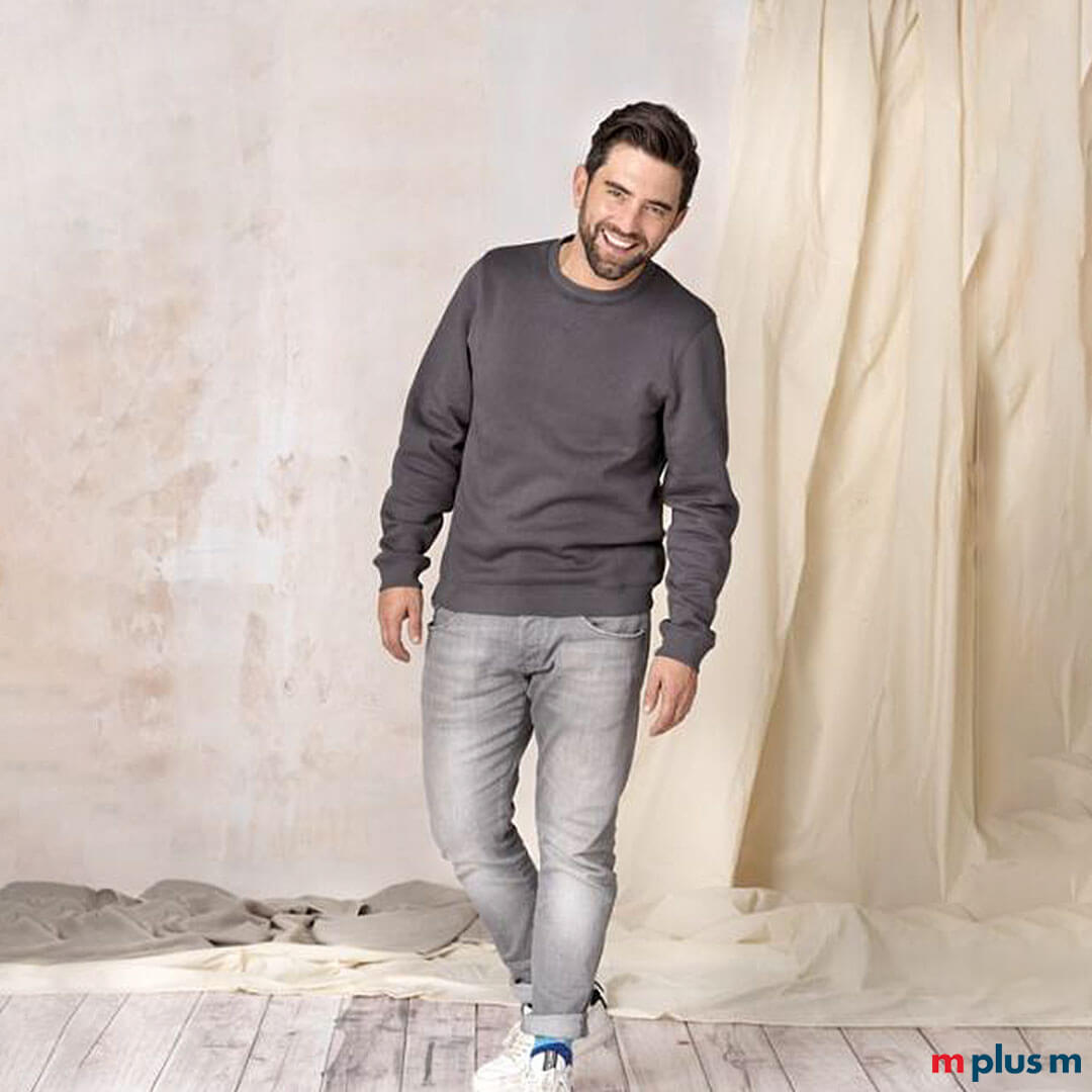 Schoner-Rundhals-Pullover-mit-eigenem-Logo-gestalten-als-Werbegeschenk-RE Model trägt graues nachhaltiges Sweatshirt. Individuell mit Logo zu bedrucken