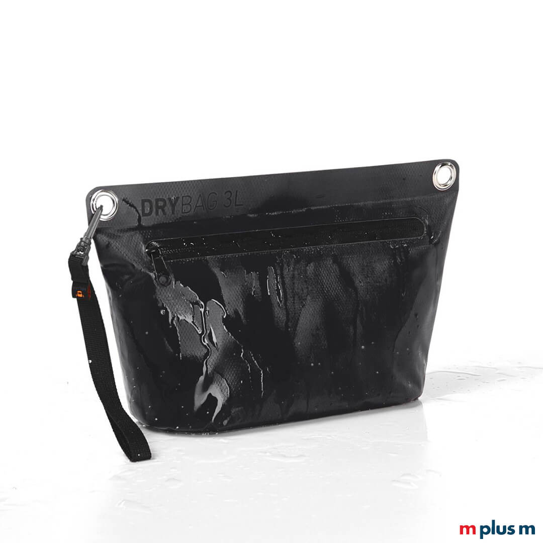 Nahaufnahme einer schwarzen 3L Drybag von Halfar mit schwarzem Reißverschluss und Handschlaufe, demonstriert ihre Wasserdichtigkeit durch darauf spritzendes Wasser. Die Aufschrift "DRYBAG 3L" ist zu sehen